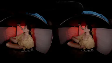 Slim brunette smokes solo in dim red-lit studio chair scene