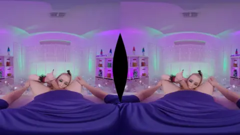 Blonde with shoulder tattoo spreads on purple bed under LED lights